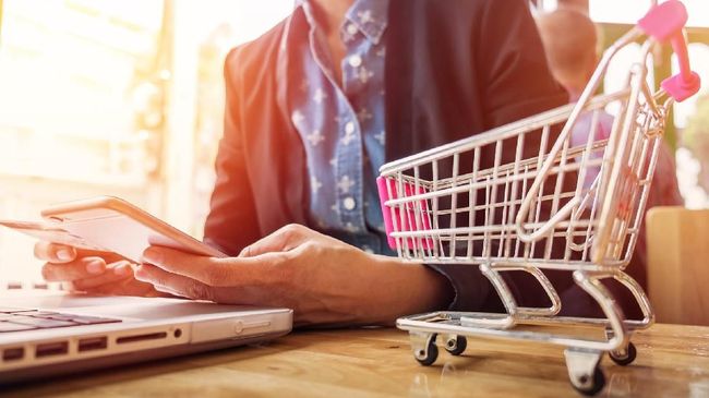Ilustrasi belanja online dengan laptop dan keranjang belanja mini, tren live shopping yang makin populer di Indonesia.