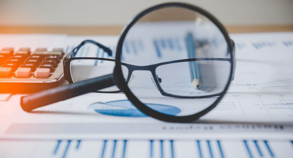 Kacamata dan grafik laporan riset pasar sebagai simbol analisis untuk mendapatkan harga terbaik sebelum membeli